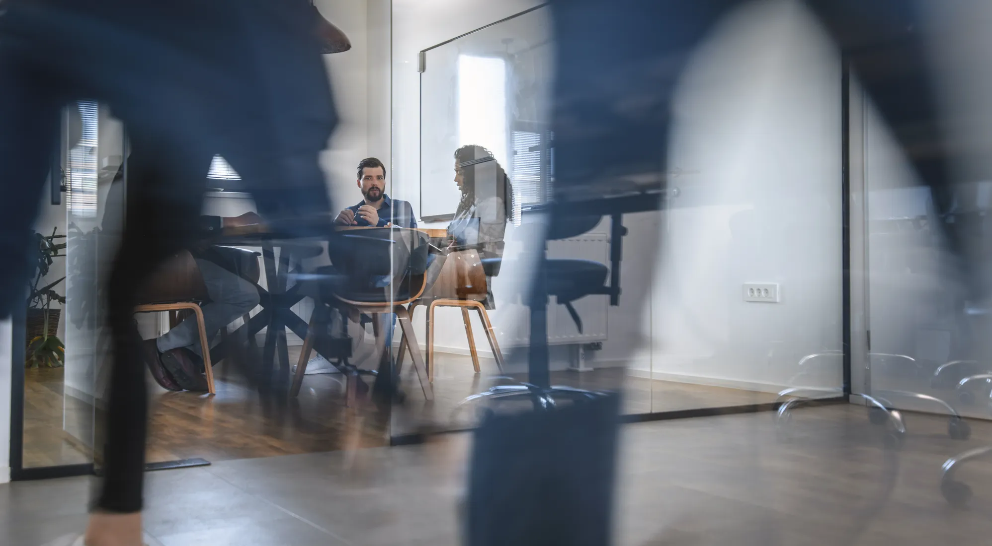 Eine unscharfe Silhouette im Anzug läuft von links nach rechts. Dahinter sitzt ein Mann auf einem Sofa.