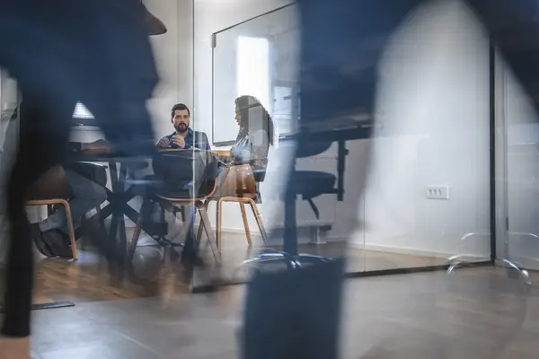 Eine unscharfe Silhouette im Anzug läuft von links nach rechts. Dahinter sitzt ein Mann auf einem Sofa.